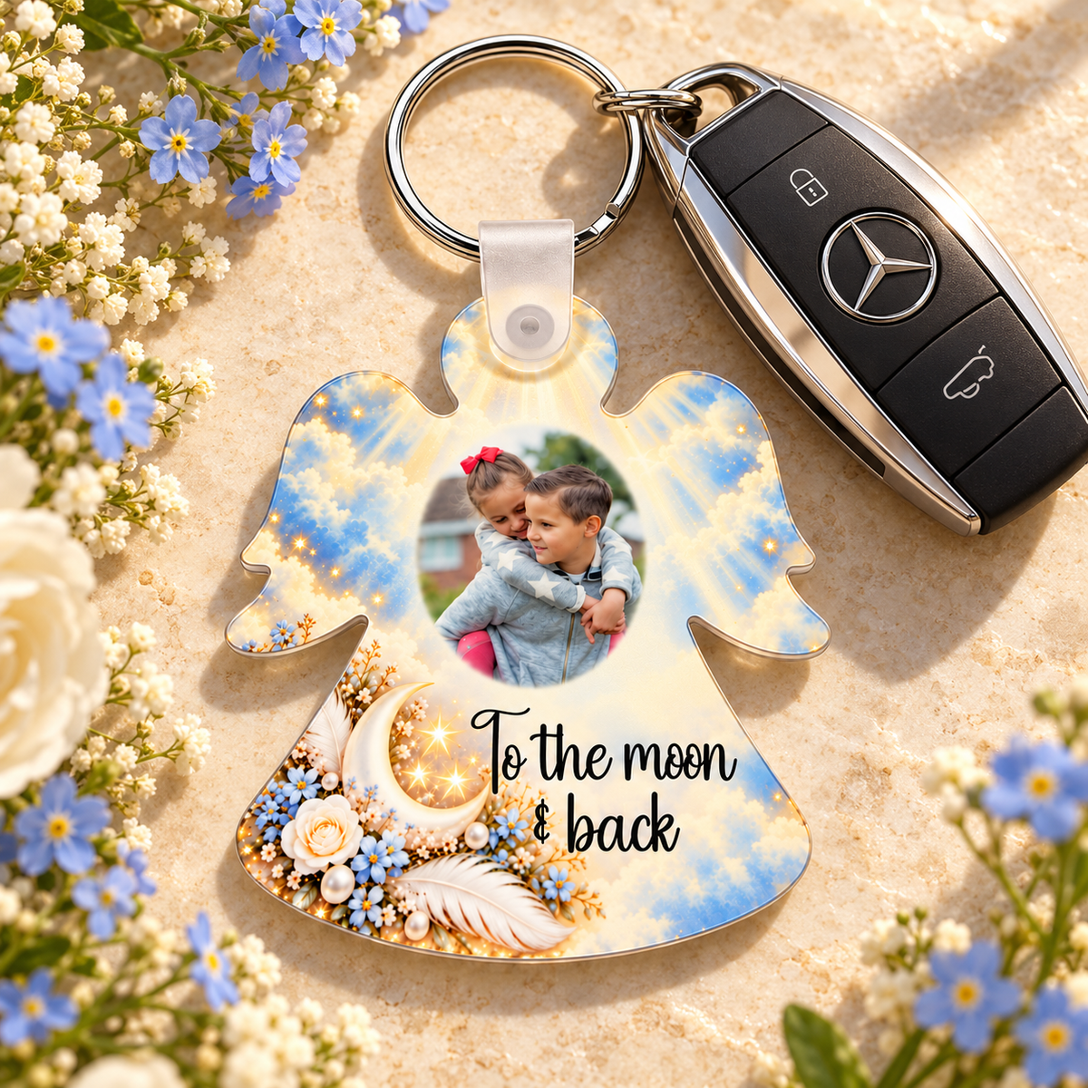 Personalised angel photo keyring beside car keys and blue flowers, featuring a crescent moon, white feather and sentimental verse
