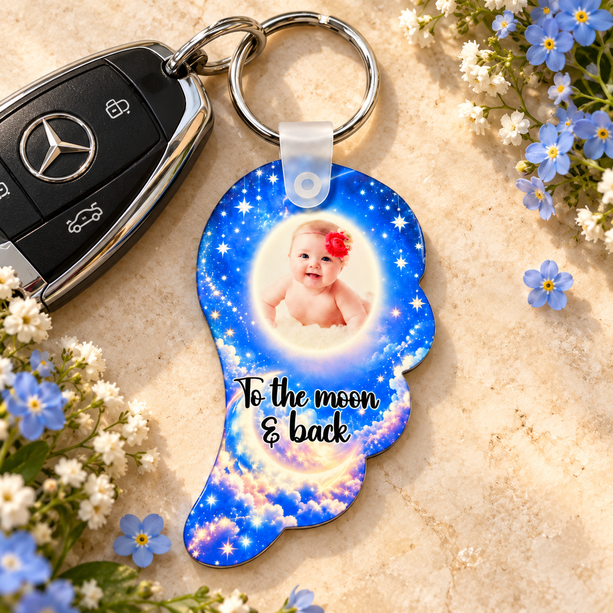 Personalised moon and stars angel wing baby photo keyring beside Mercedes car keys and blue flowers