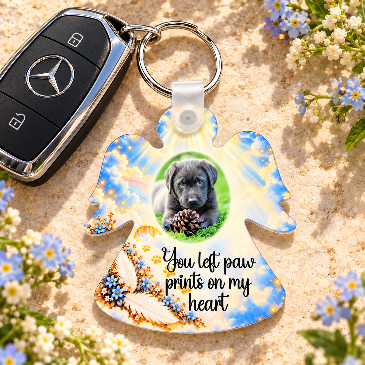 Personalised pet remembrance angel keyring beside car keys and blue flowers, featuring a dog photograph and paw prints memorial verse