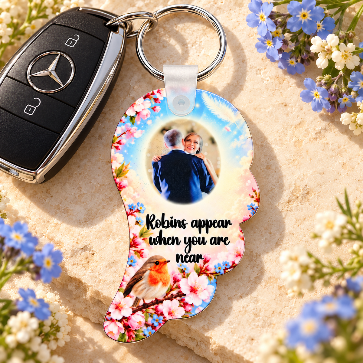 Personalised robin angel wing remembrance keyring beside car keys with blue forget-me-not flowers