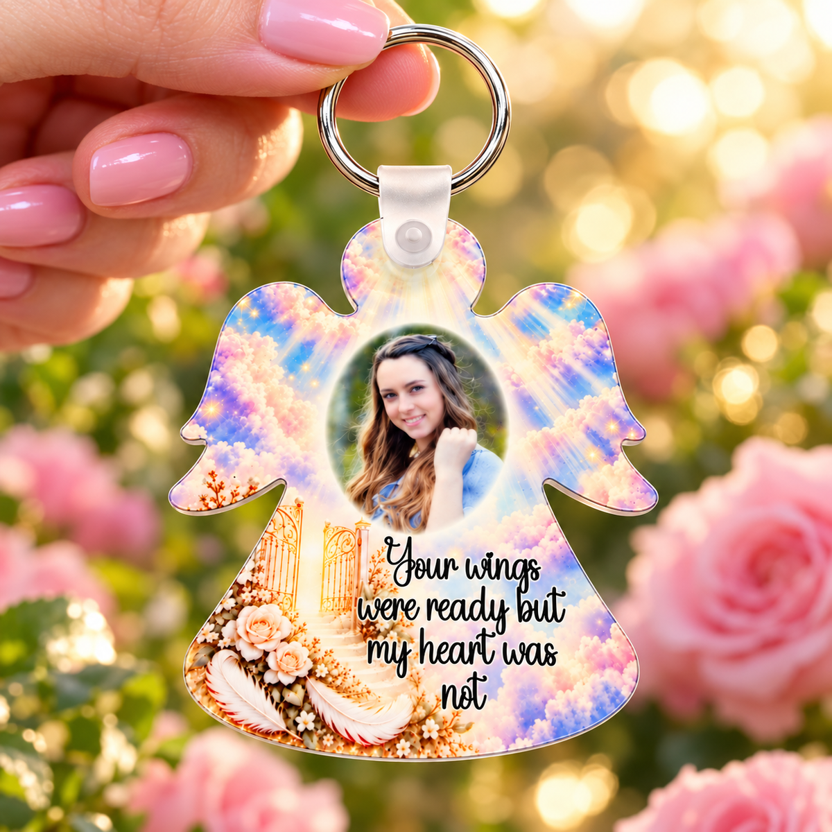 Personalised angel memorial photo keyring held against soft pink roses and fairy lights, featuring heavenly clouds and golden gates