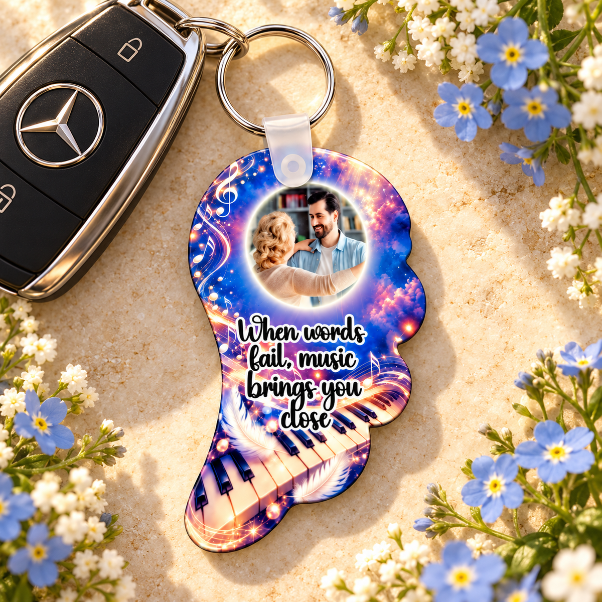 Personalised musical angel wing remembrance keyring beside car keys with blue forget-me-not flowers