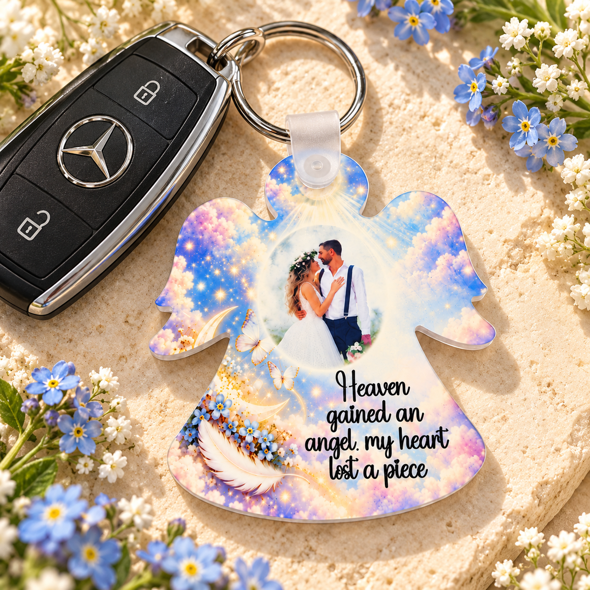 Personalised memorial angel keyring beside car keys and blue forget-me-not flowers, featuring a photograph and heavenly cloud design