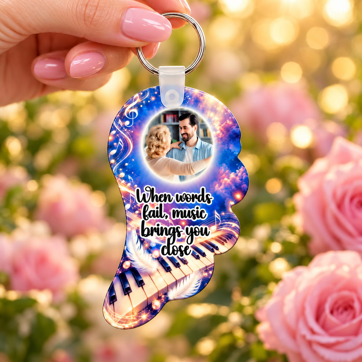 Blue and purple music memorial angel wing photo keyring held in hand against a soft pink floral background