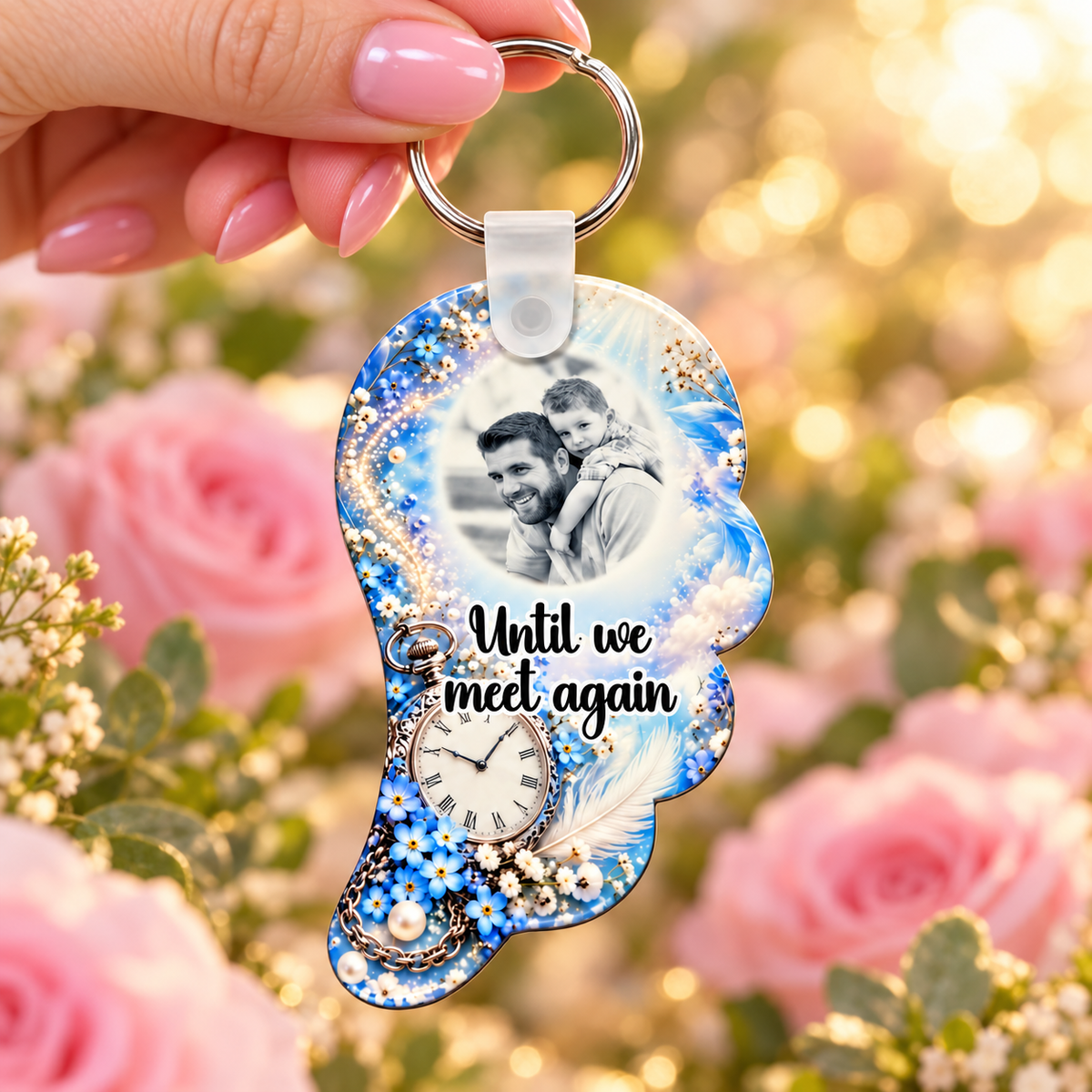 Blue memorial angel wing photo keyring held in hand against a soft pink rose background